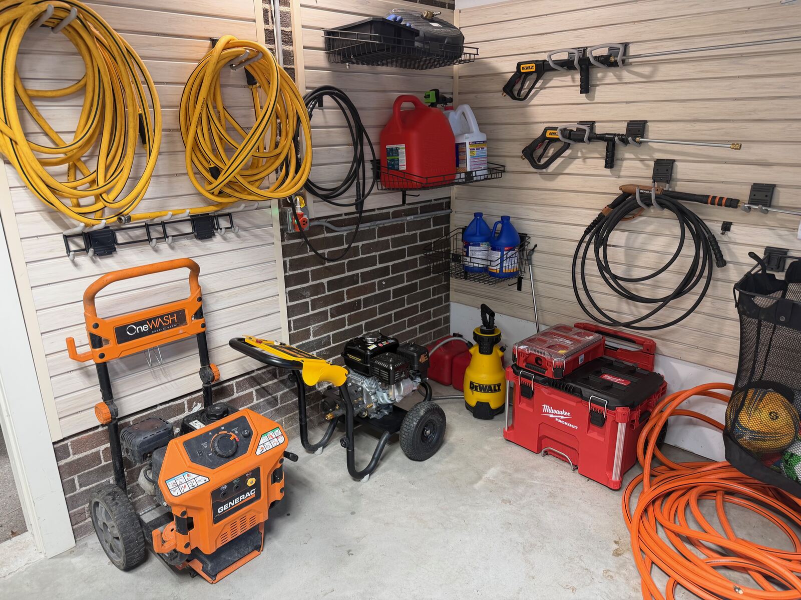 Full equipment storage wall with multiple pressure washers, hoses, and backup generator